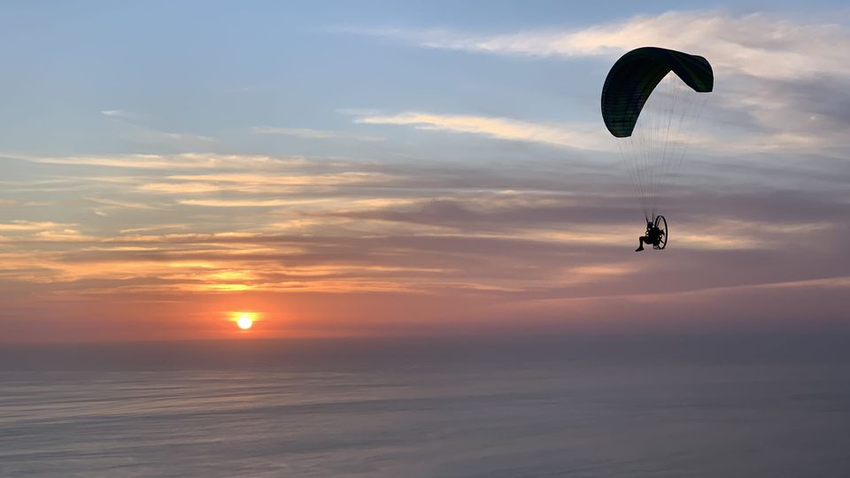 Paramotor silhouetted against a low sun over the ocean